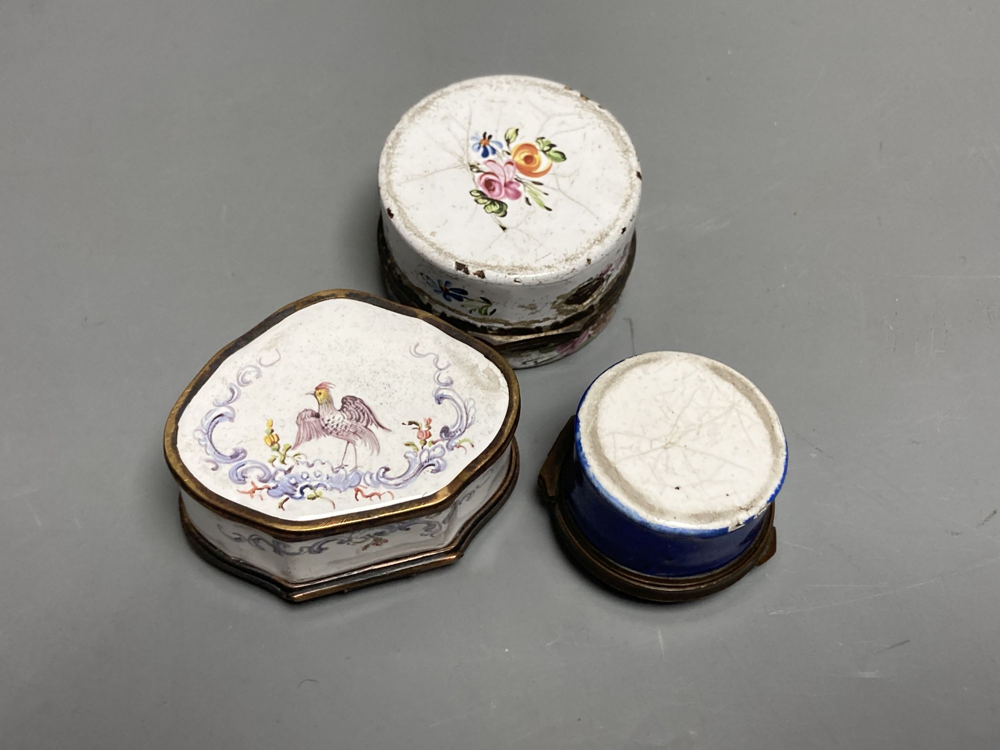 An 18th century white enamelled box painted with a palace, 5cm., a cartouche shaped box decorated with a birds, 6cm. and a patch box de